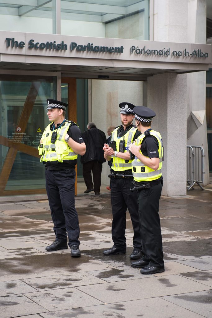 3 police scotland officers standing outside parliament in Edinburgh