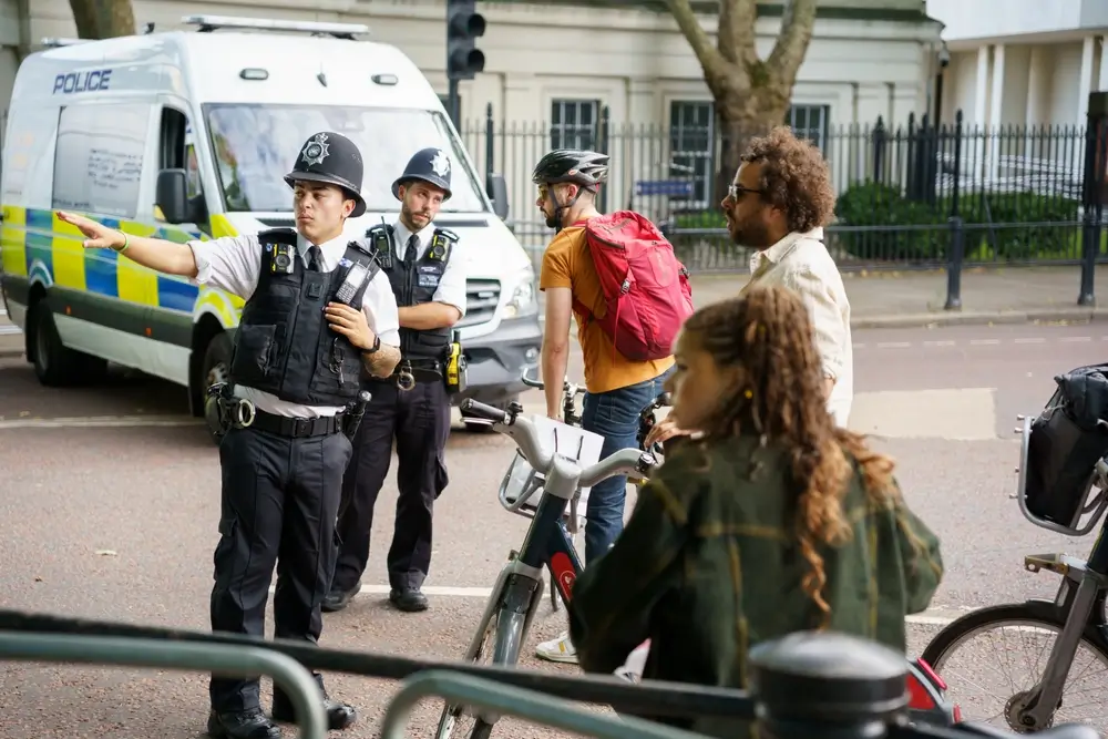 Police officer patrolling community, providing directions to people on bicycles next to a parked police van.