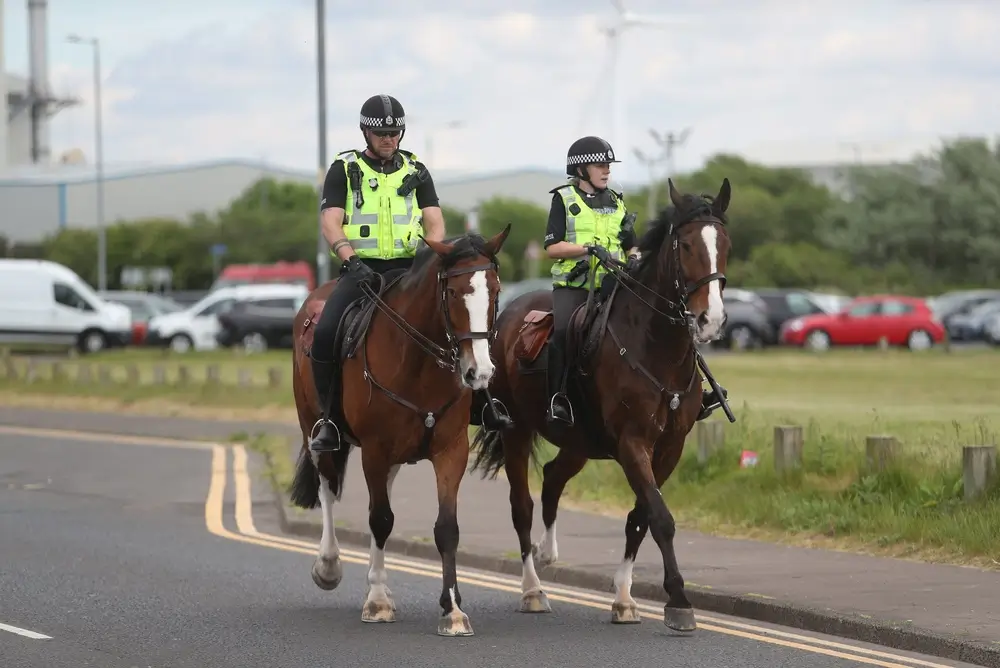 Two mounted Scottish police officers on patrol, wearing high-visibility vests and helmets.