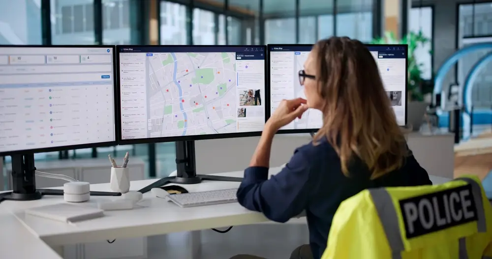 Police IT specialist monitoring digital crime maps on three screens, providing IT support and utilizing police technology.