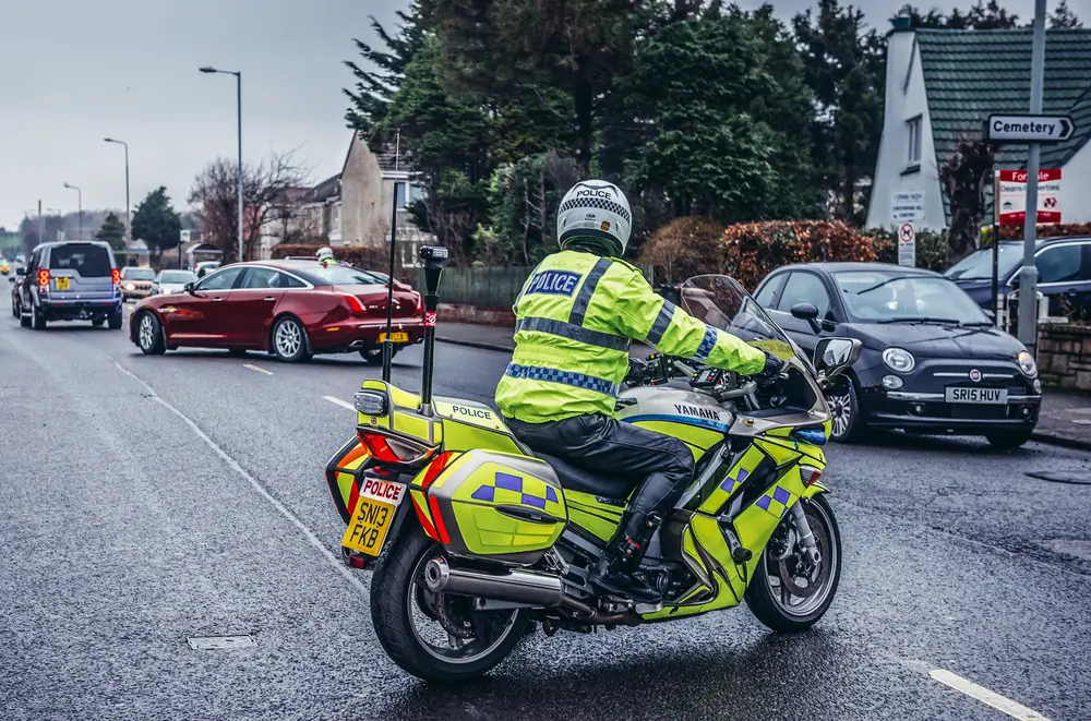 Scottish police officer on a marked police motorcycle patrolling a residential street.